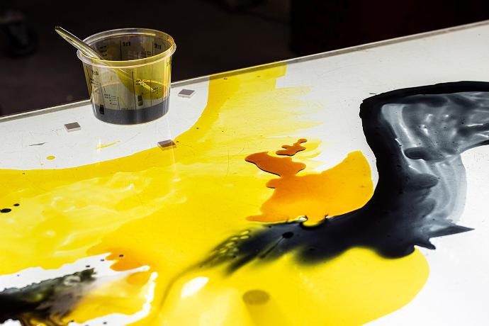 Razlivena žuta i crna tekućina i posudica s bojom i kistom na osvijetljenoj površini