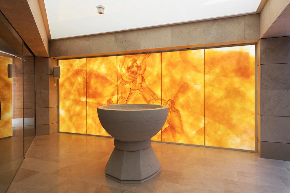 Room lined with stone, with a painted glass wall and stone baptistery. 